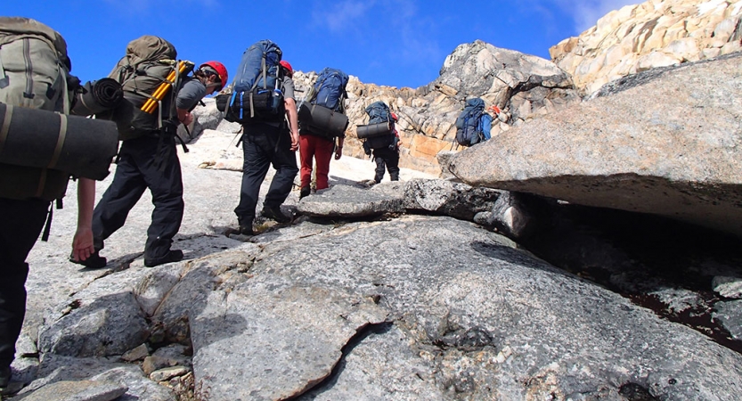 A group of people wearing backpacks hike up a rocky incline. 